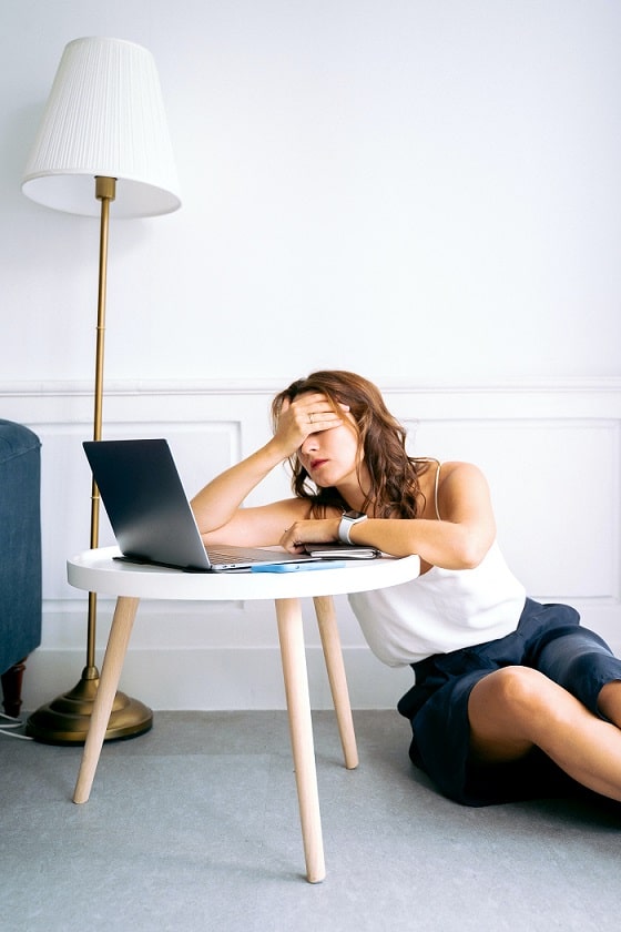 mujer con la mano en los ojos frente a una laptop